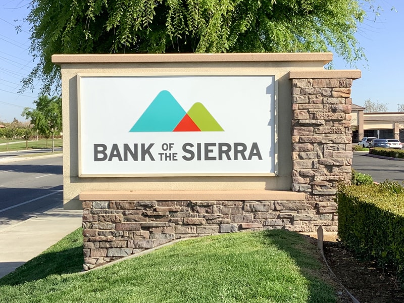 Bank of the Sierra architectural monument sign in Bakersfield, CA featuring a stone masonry base, stucco columns, and an illuminated cabinet face for high daytime and nighttime visibility.
