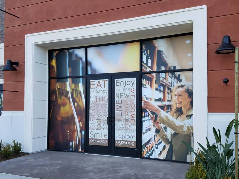 Custom storefront window graphics featuring lifestyle photography and promotional messaging for Oakwood Communities’ wine store in Oxnard, CA.